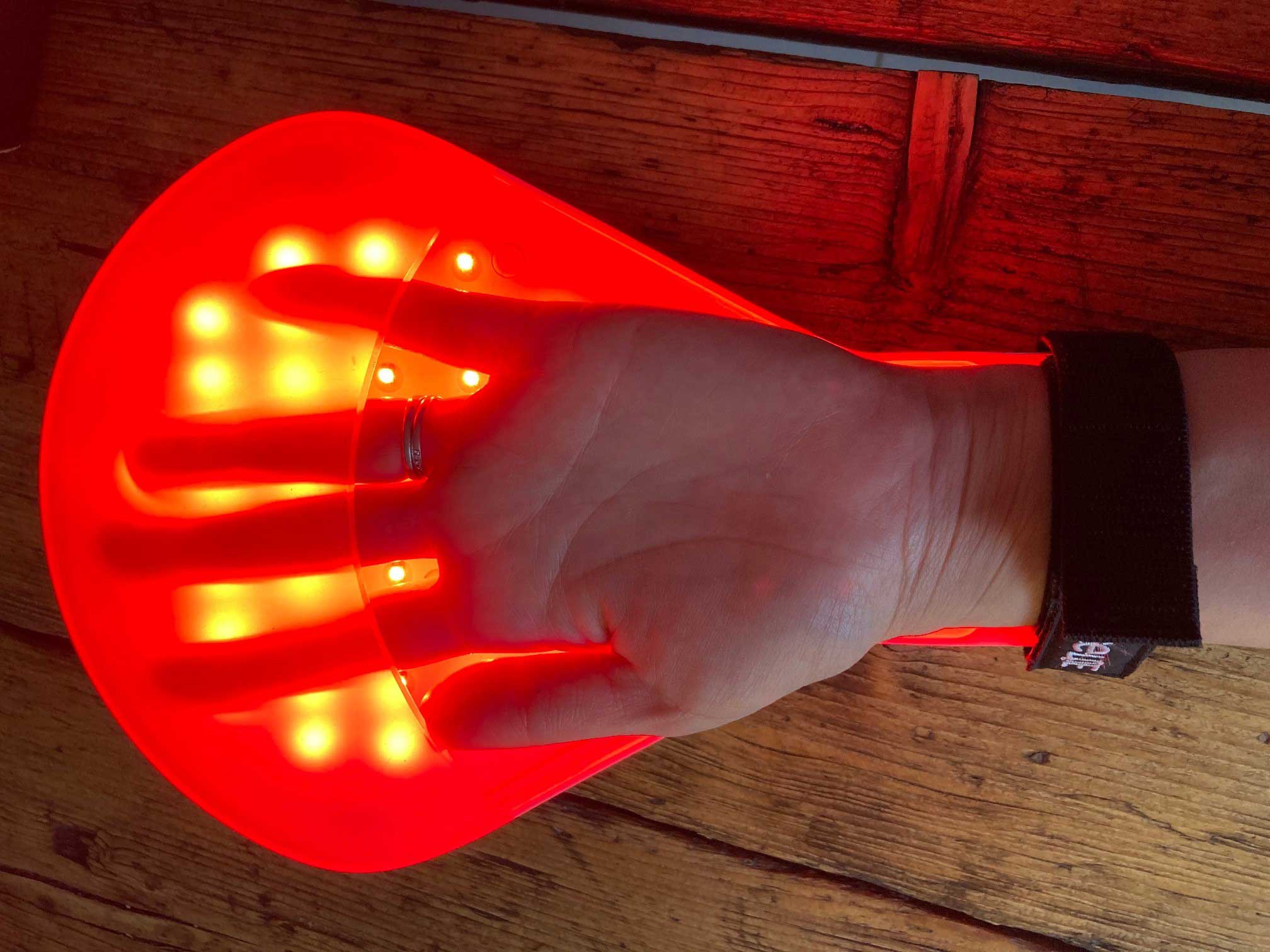 Hand receiving red LED light therapy inside flexible glove handLITE device