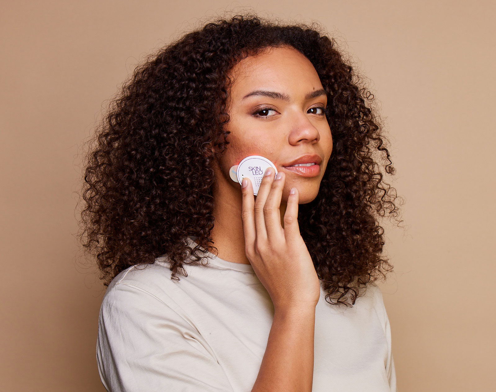 Model applying SkinLED handheld red light therapy device to cheek