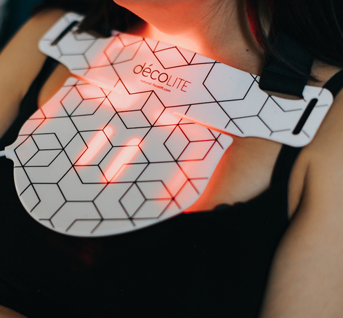 Décolite LED neck light therapy device glowing red on model’s chest