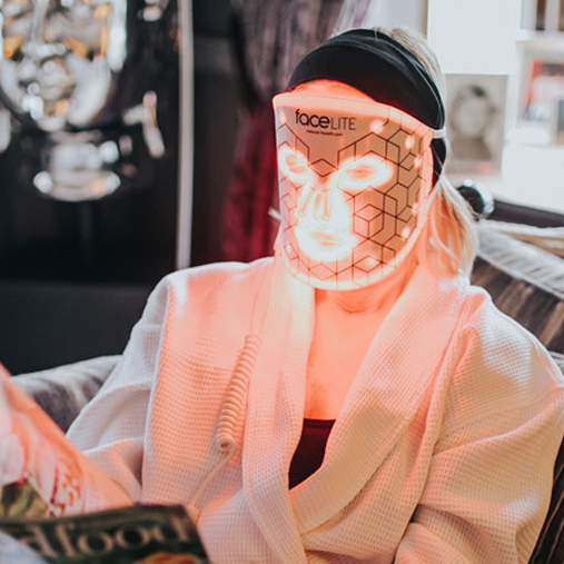 Person wearing FaceLite LED light therapy mask while relaxing at home